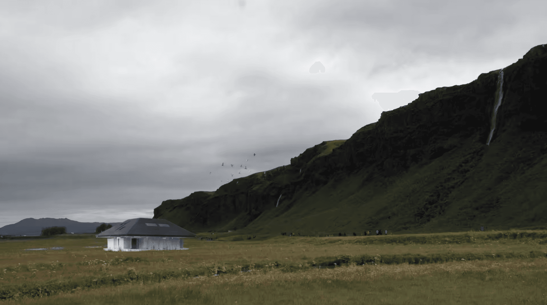 Courtyard house placed in an open Icelandic landscape beneath a long mountain ridge