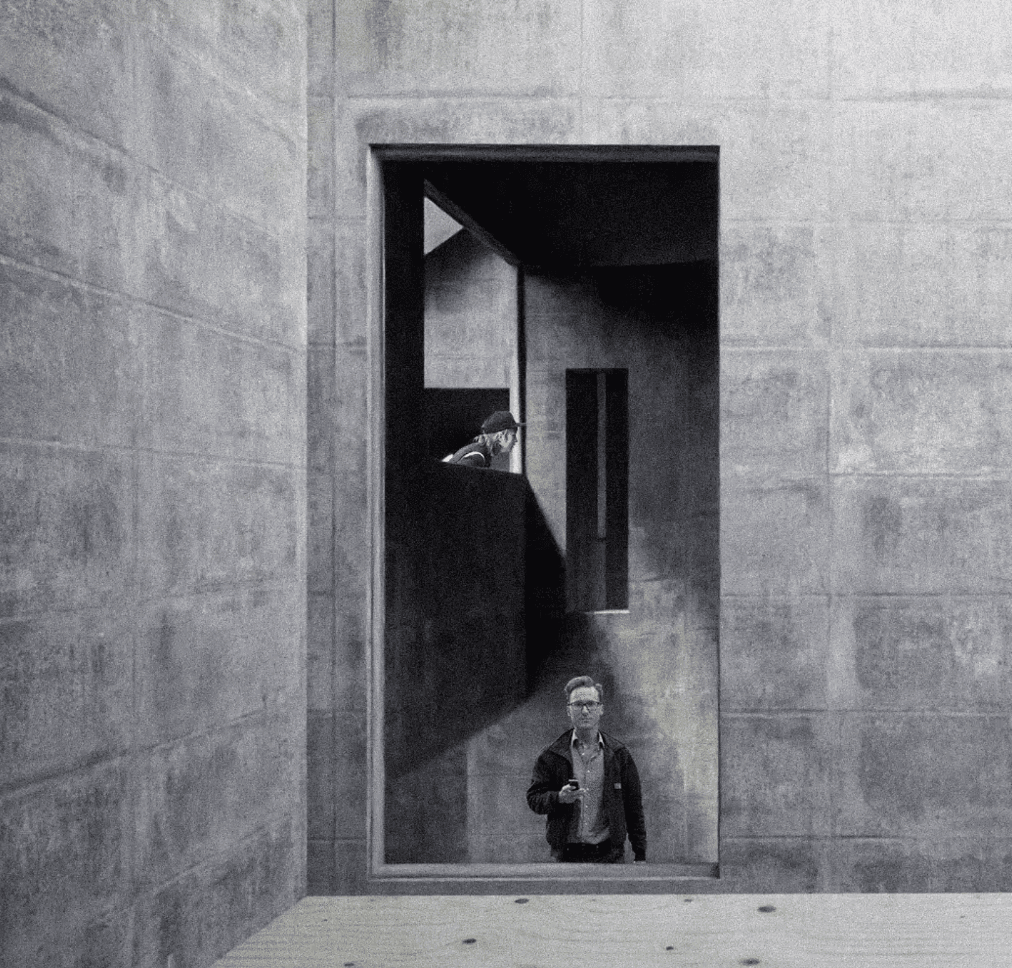 Deep rectangular opening in a thick concrete wall, with people on either side of the threshold