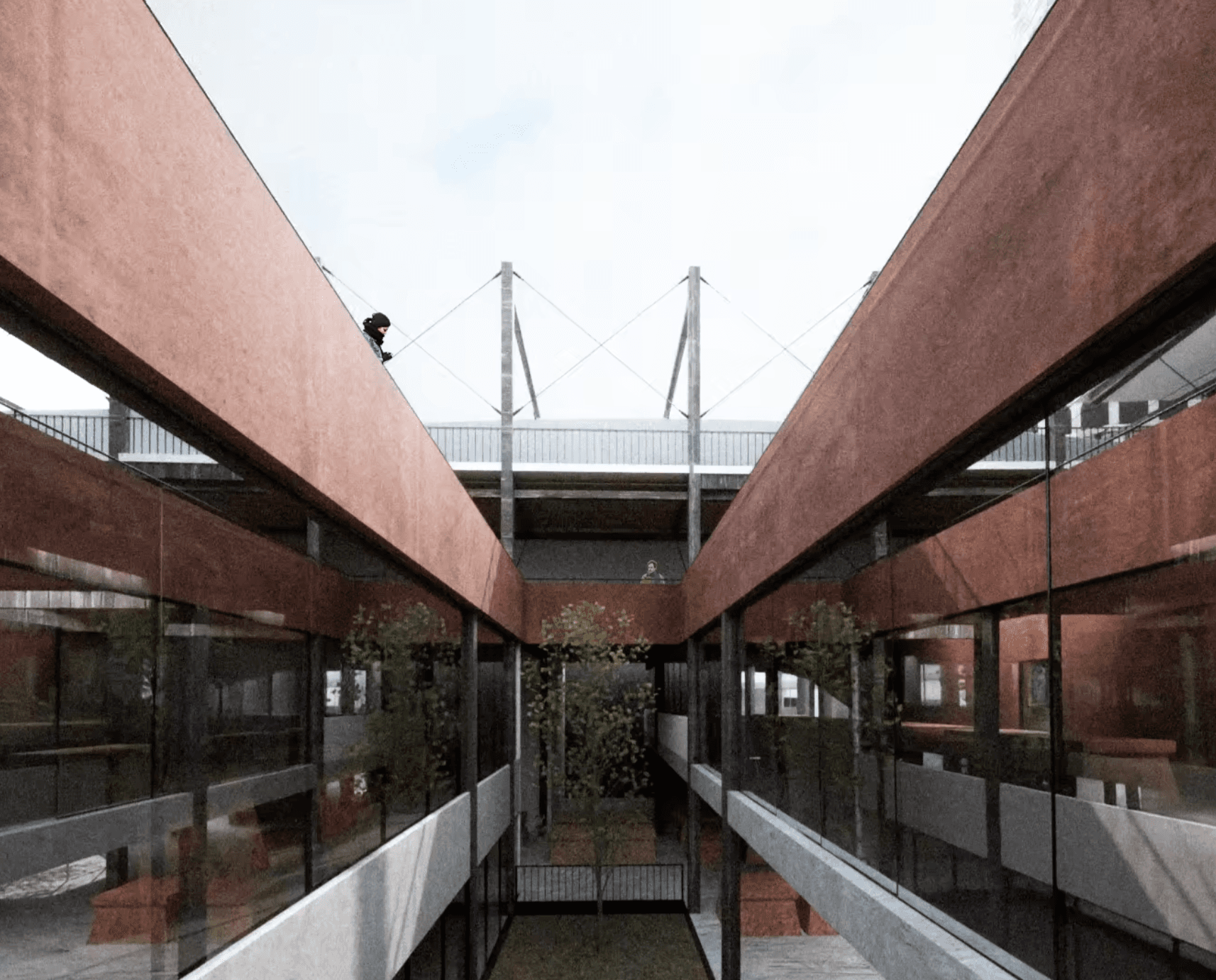 View into an open courtyard between red walls and glazed galleries, with a bridge and structural frame overhead
