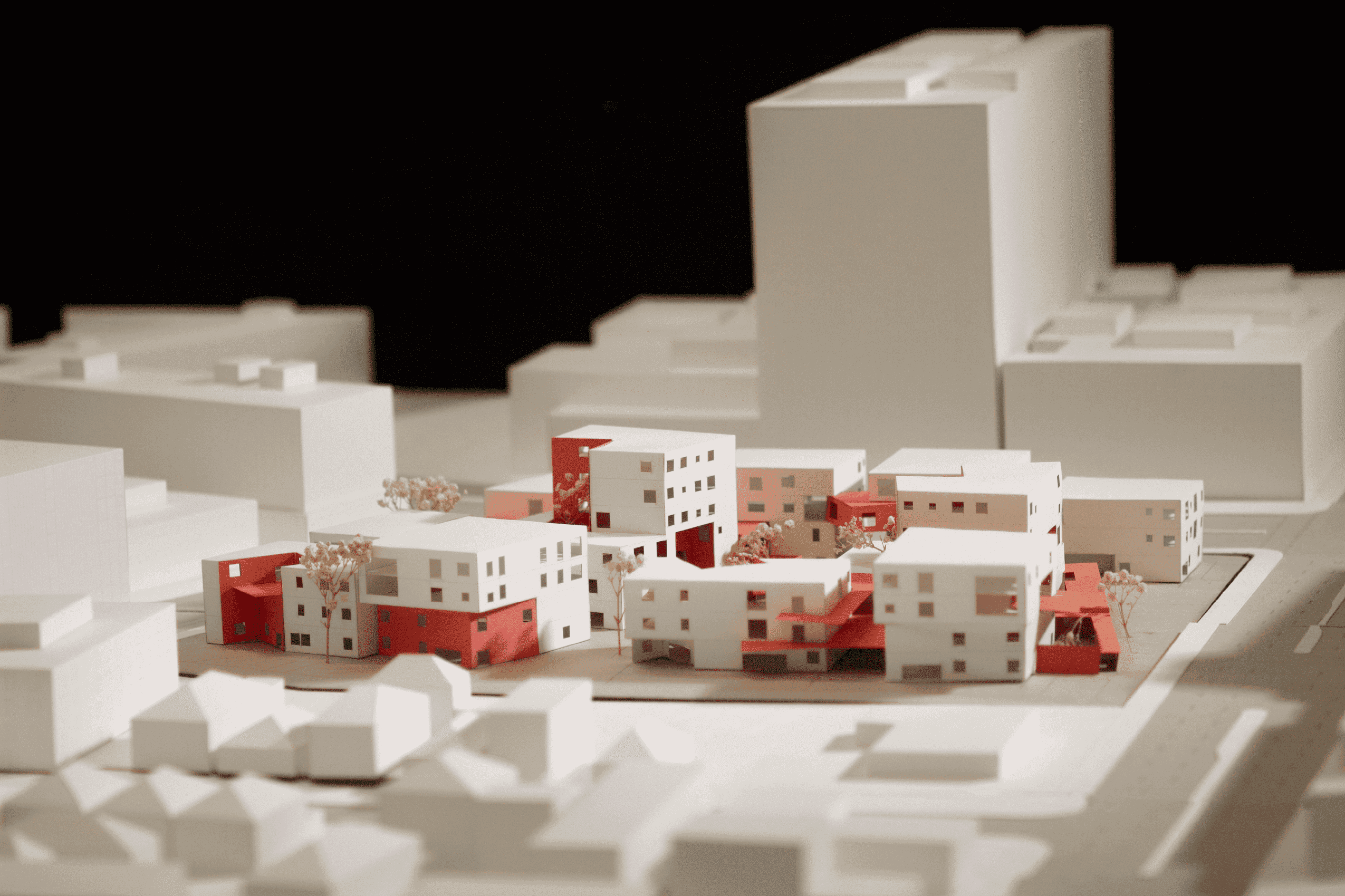 Physical model of white residential blocks with red connecting volumes, planted courtyards, and surrounding Oakland buildings