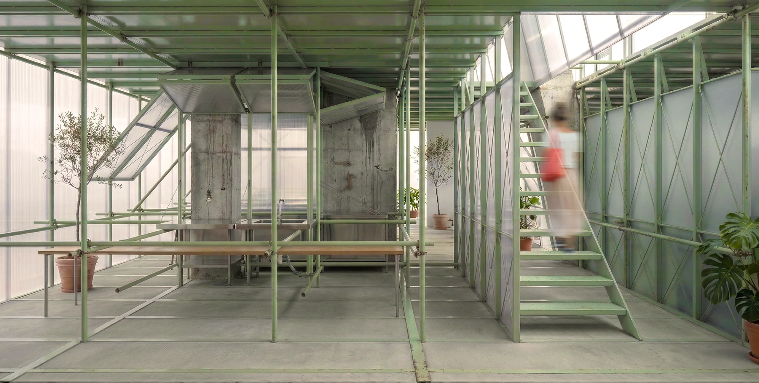 Interior view of a green secondary frame inserted among concrete columns, with a stair, planting, and shared tables